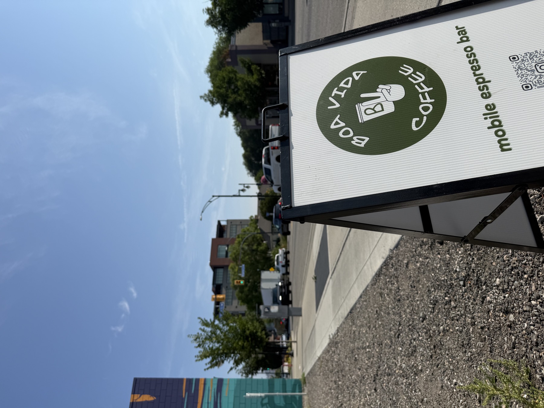 The Boa Vida Coffee A-frame sign on a downtown Kelowna sidewalk, mural building behind