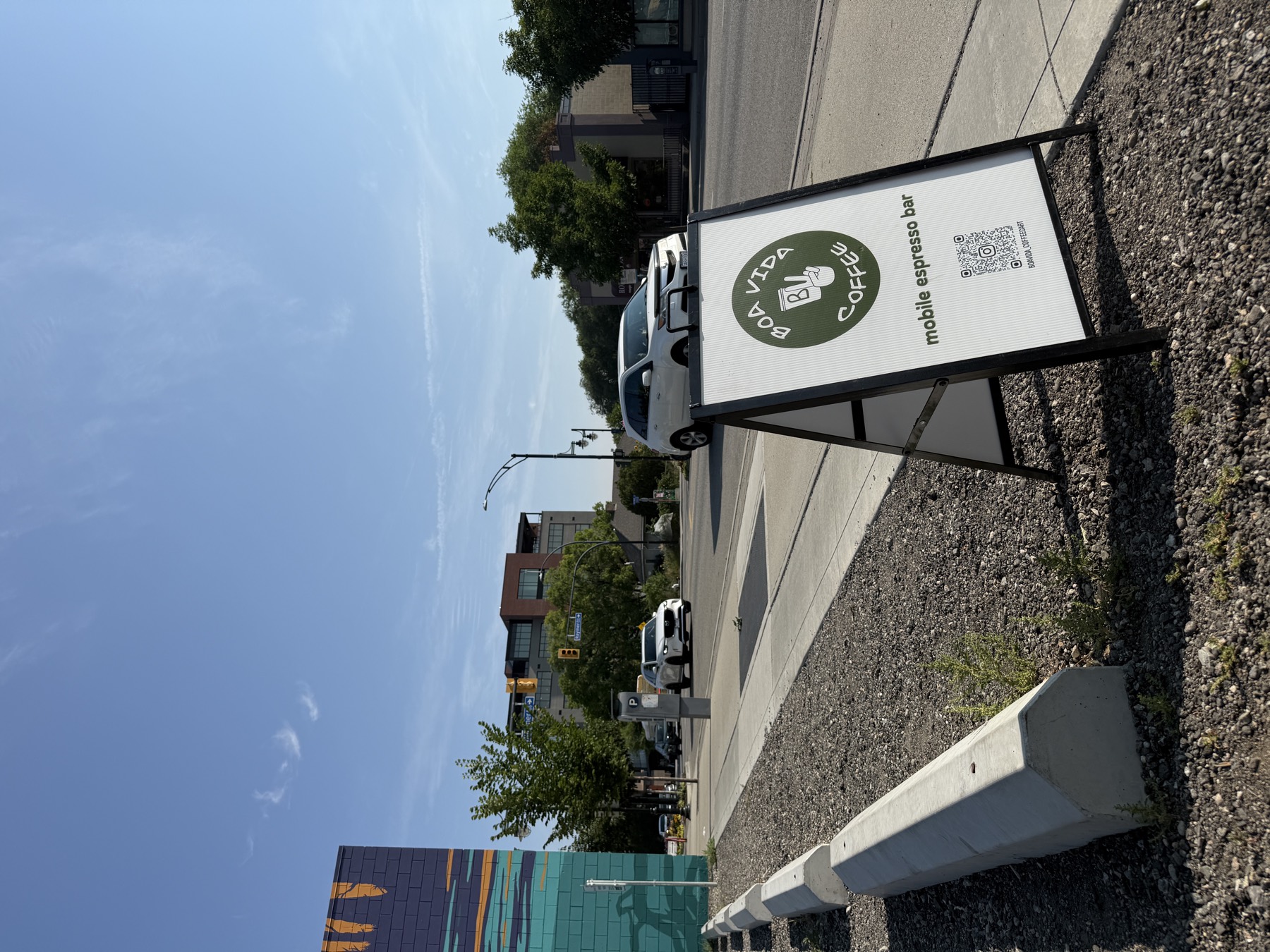 Boa Vida Coffee A-frame sign on a Kelowna sidewalk with the downtown mural behind