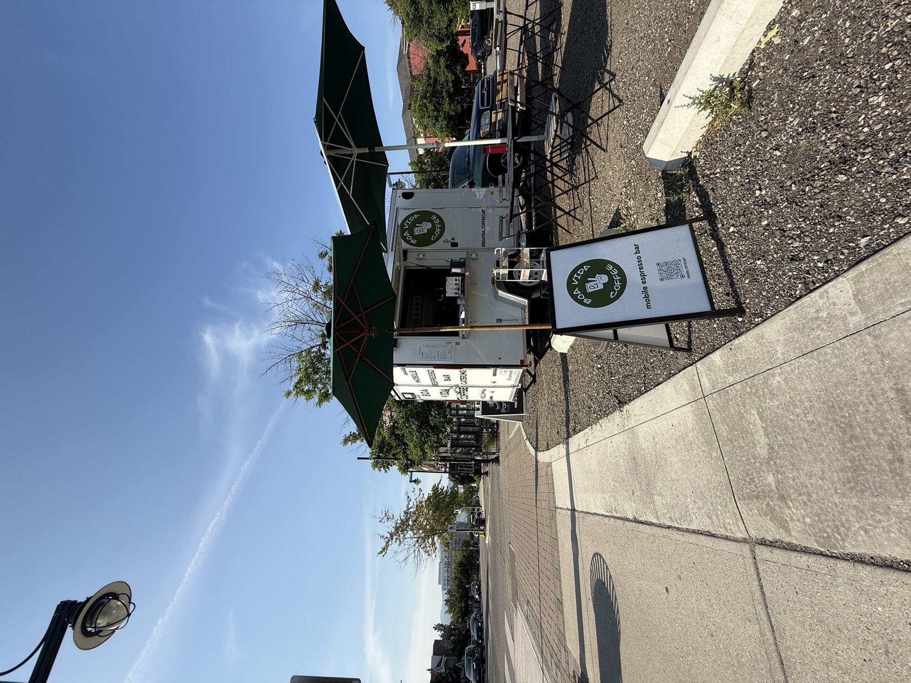The Boa Vida Coffee trailer set up curbside with green umbrellas and cafe tables in downtown Kelowna